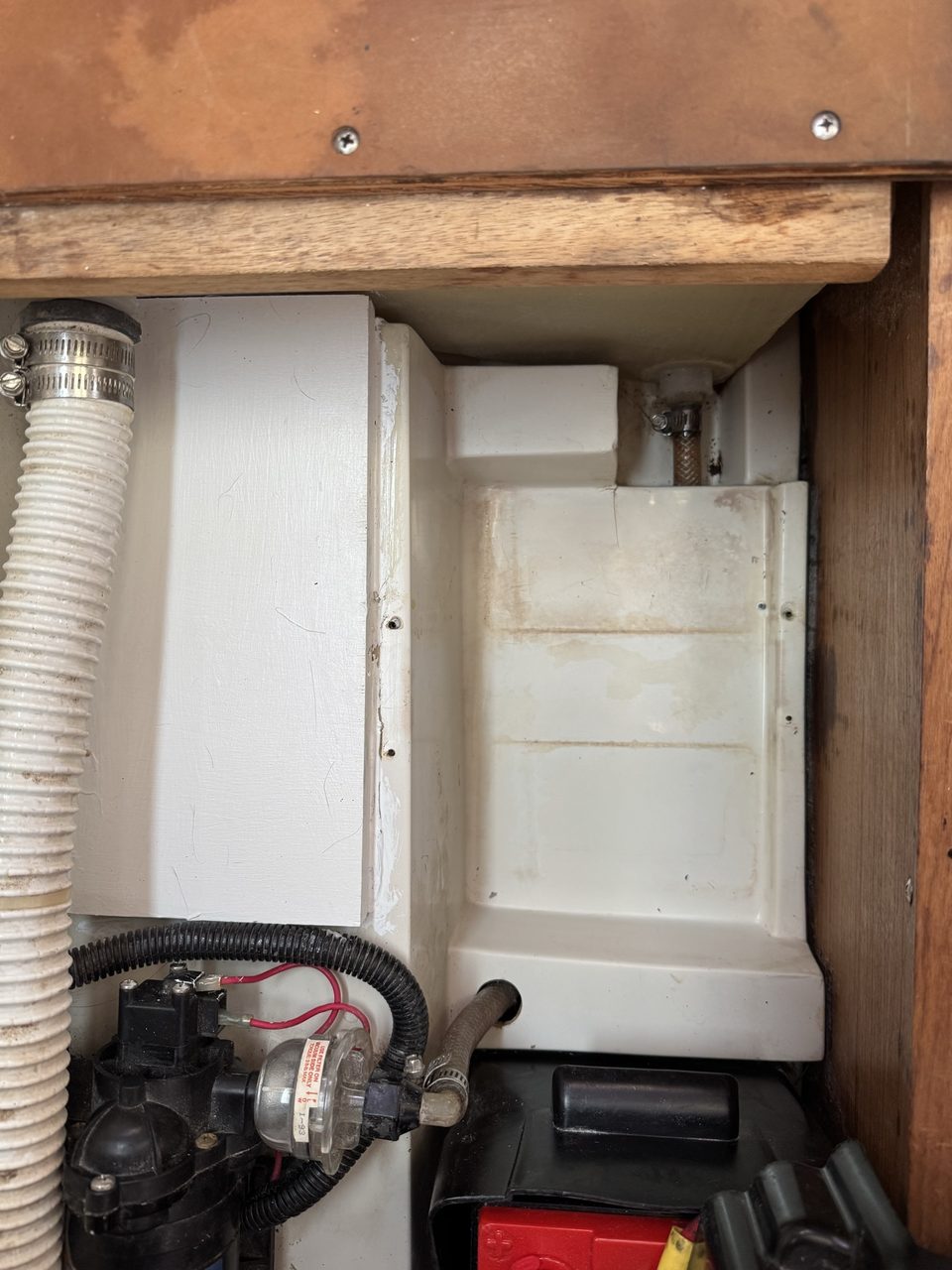The same battery compartment cleaned out, with plumbing and a pump on the left and an old battery visible at the lower right
