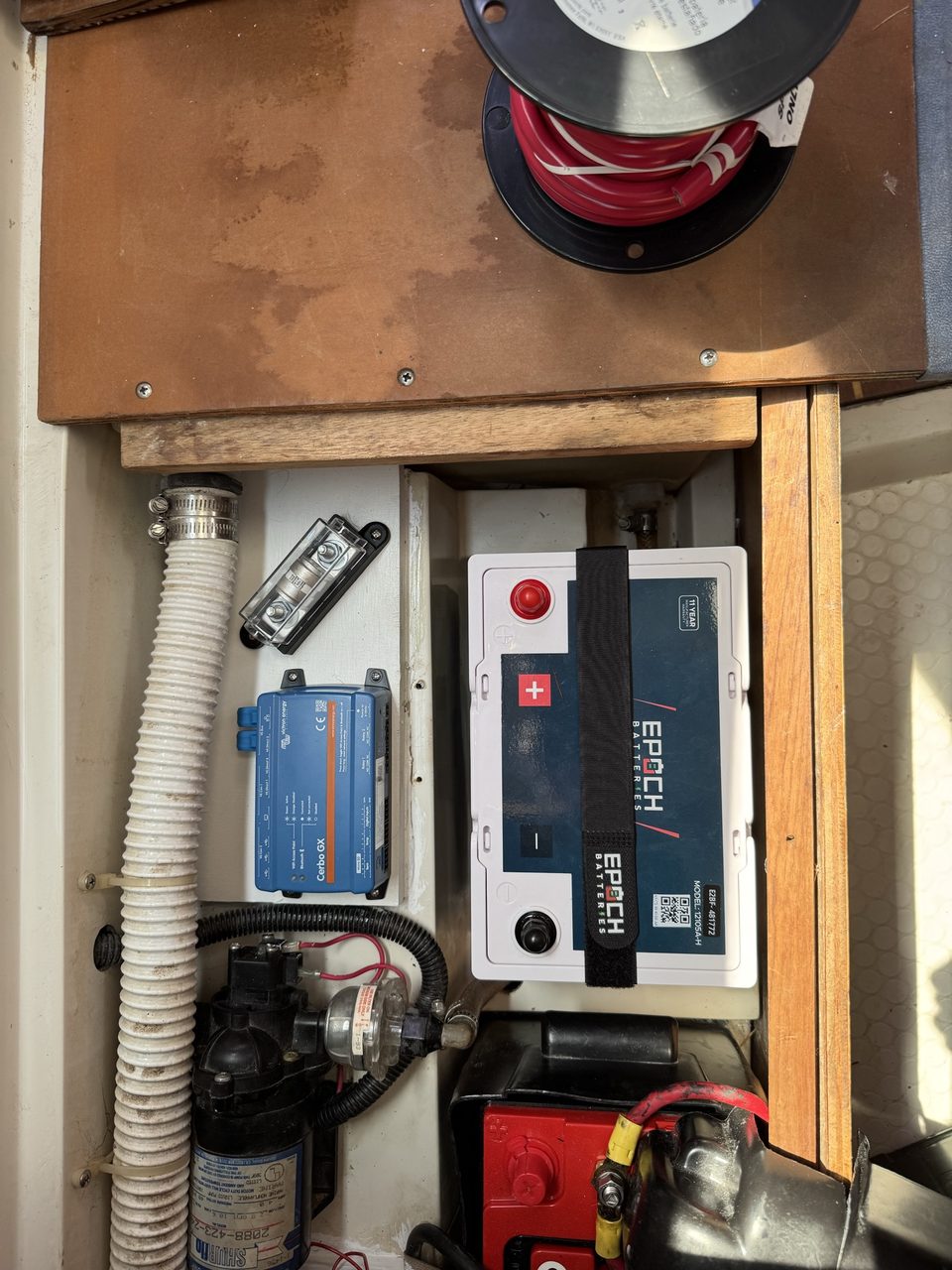 A boat battery compartment showing a large fuse holder and a blue Victron control unit mounted on a white painted board