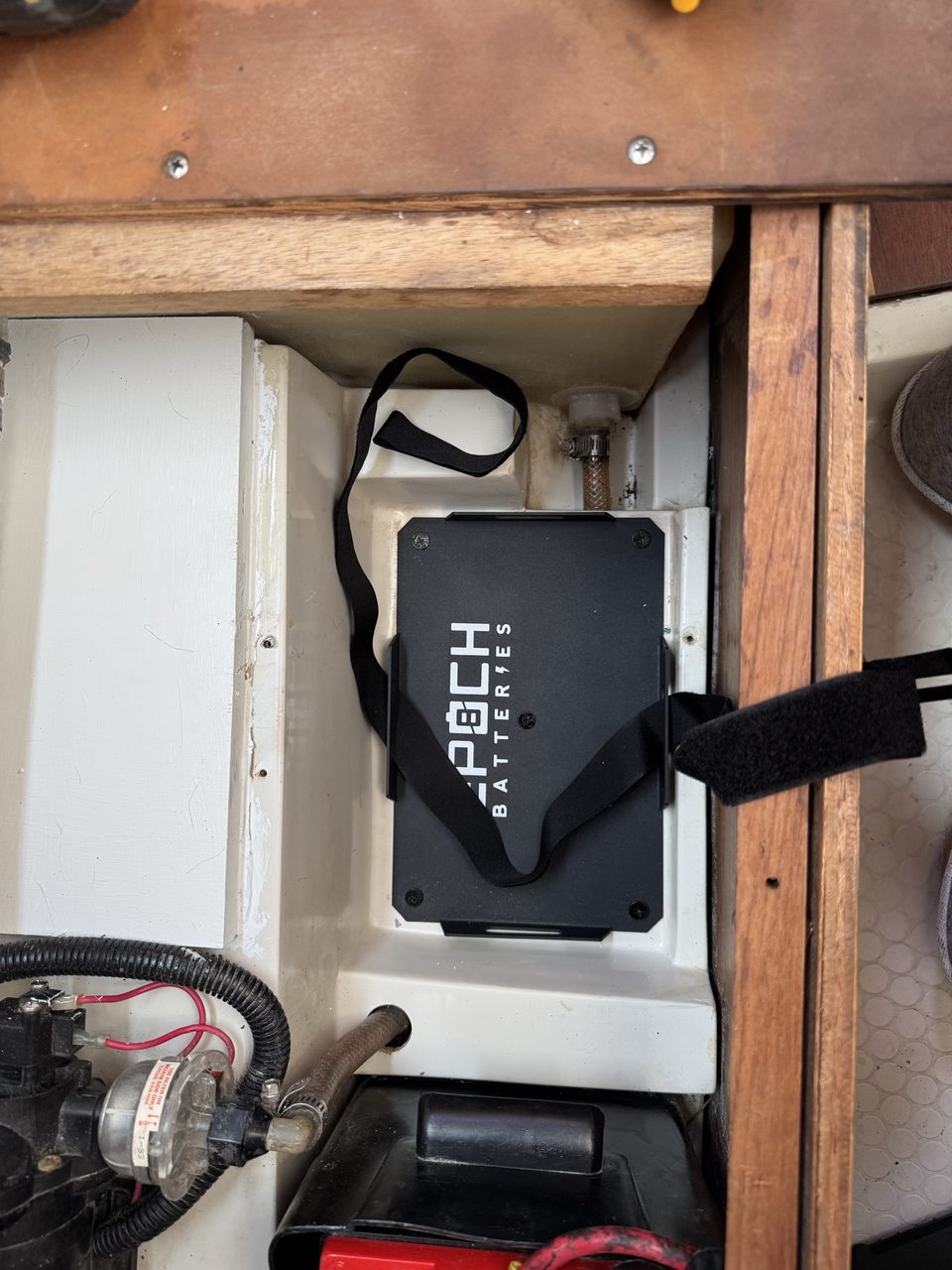 A black battery tray screwed down into a cleaned battery compartment, with webbing straps laid ready either side of it