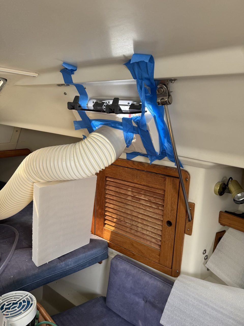 A block of white polystyrene foam taped into a boat port light with blue masking tape, with a flexible duct passing through it