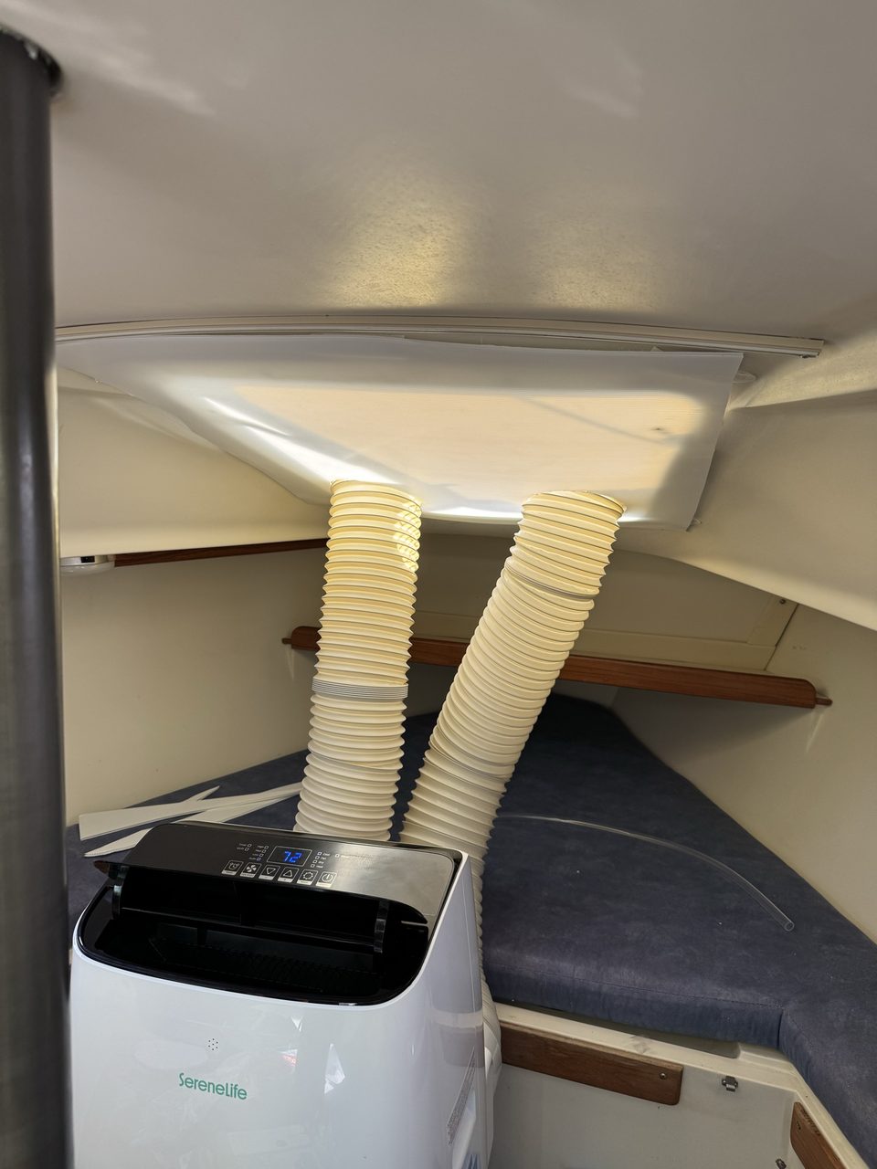 The same panel with the tape removed, two ducts rising through it, and a portable air conditioner below showing 72 on its display