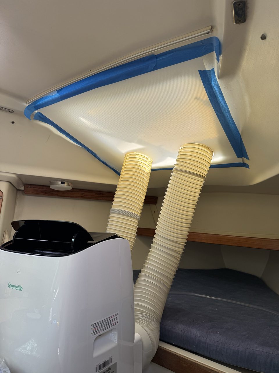 A white plastic sign board taped to the deckhead of a boat cabin over an open hatch, with two flexible ducts passing through holes in it