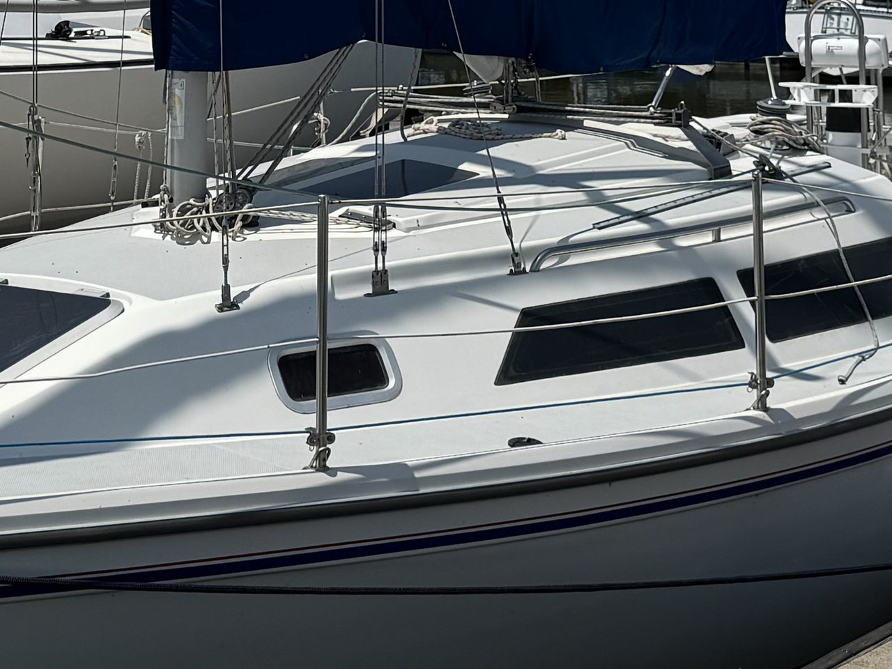 Outside, from the dock. Three shroud terminals along the coachroof edge, the handrail inboard of them, and the same portlight below.