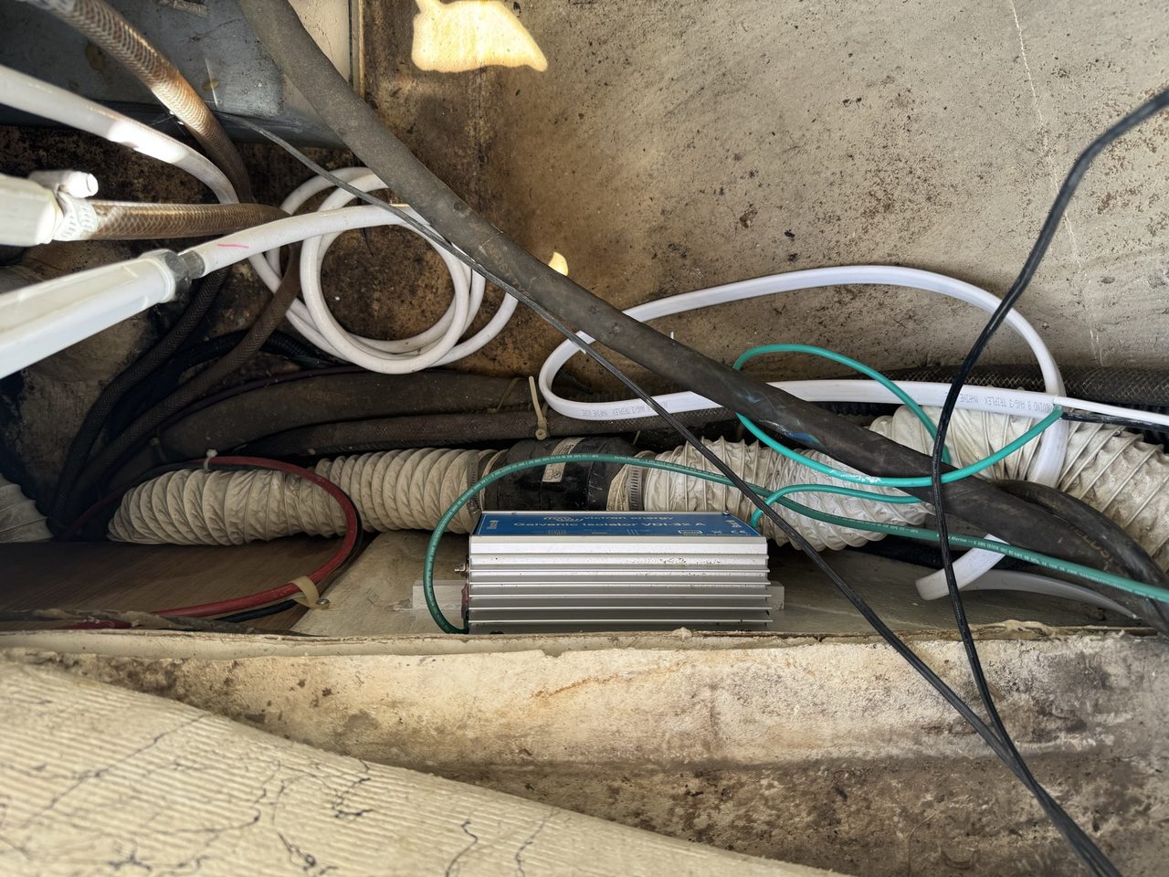 Looking down into the lower half of a cockpit locker, with the galvanic isolator mounted low and hoses and cables running across the space
