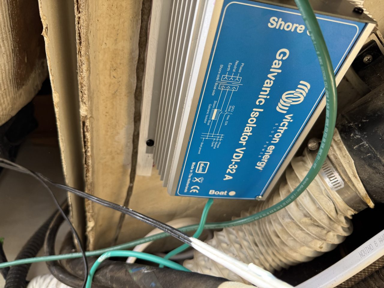 A blue and silver Victron VDI-32 galvanic isolator screwed to white-painted wooden battens inside a locker