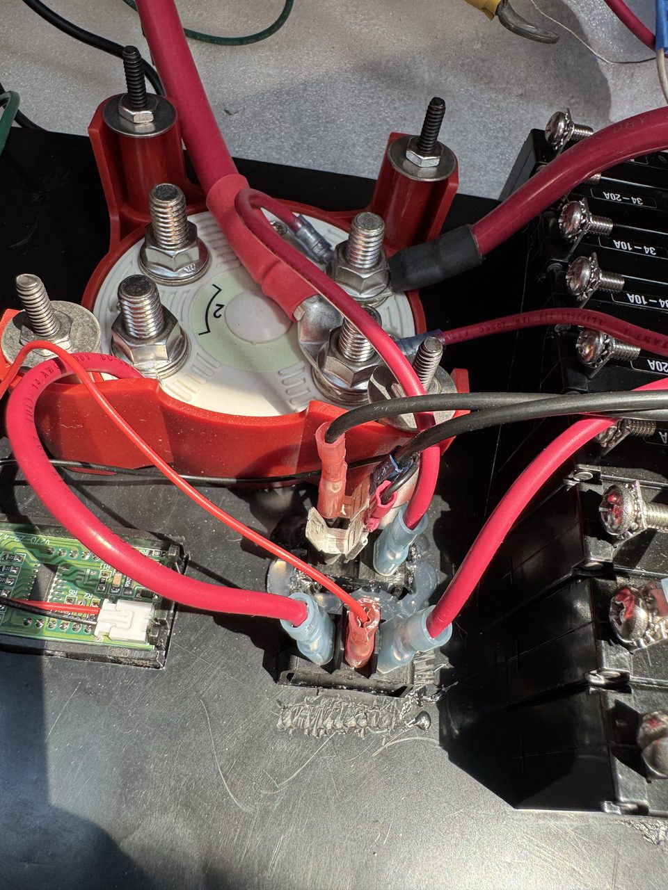 Close-up of the back of a boat battery switch with heavy red cables on its studs, and below it a small black component carrying several spade terminals, one of them empty