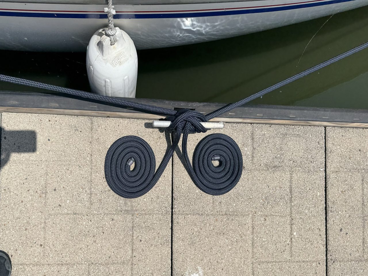 Two dock lines coiled into flat spirals on the dock either side of a cleat, with Swallow's topsides and a fender above